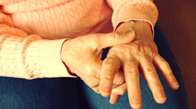 Senior woman grasps painful hand caused by arthritis