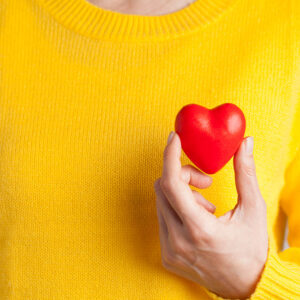 Picture of someone in a yellow shirt holding a red plastic heart.