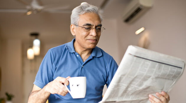 Man drinking a drink and reading the newspaper.