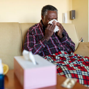 man sick on couch blowing nose.