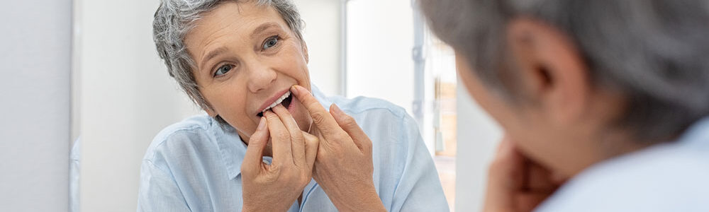 Woman flossing teeth in mirror.