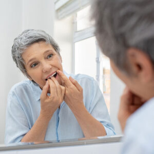 Woman flossing teeth in mirror.