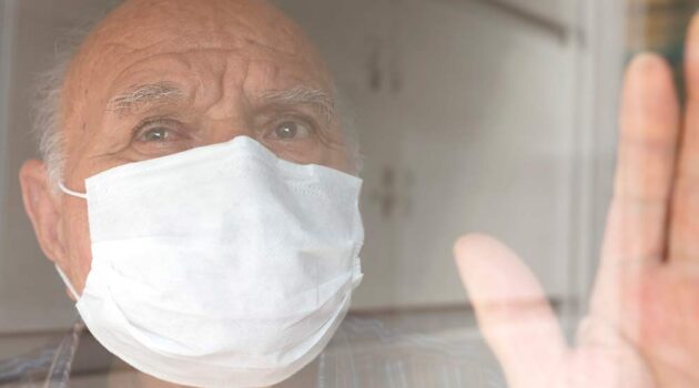 Man with mask on looking out window.