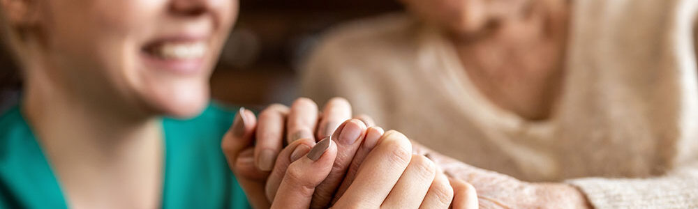 Older and younger woman smiling holding hands.