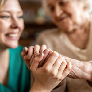 Older and younger woman smiling holding hands.