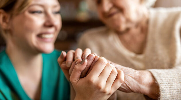 Older and younger woman smiling holding hands.