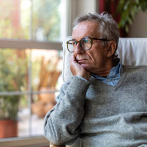 Senior man experiencing depression gazes out window.