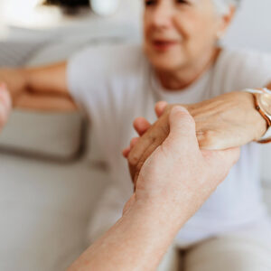 Soft focus photo of senior woman who has lost muscle being helped up from sitting on a sofa.