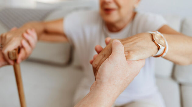 Soft focus photo of senior woman who has lost muscle being helped up from sitting on a sofa.