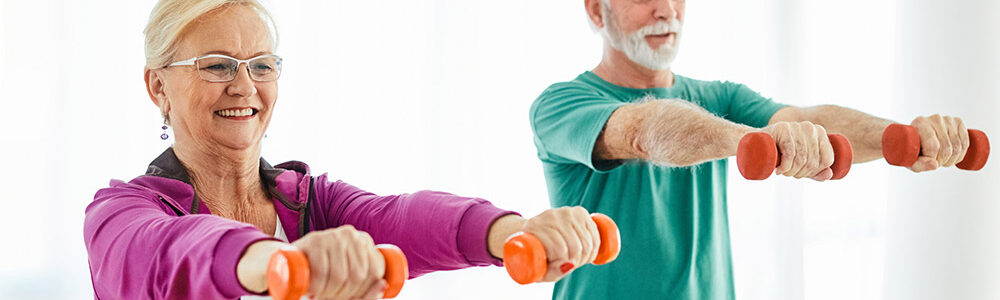 Senior man and woman arms outstretched holding small hand weights to build muscle.