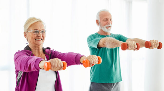 Senior man and woman arms outstretched holding small hand weights to build muscle.