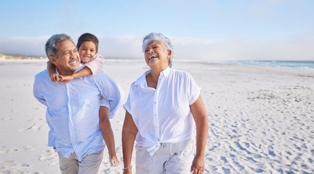 Laughing grandparents with grandchild on beach will live longer happy lives with healthy habits