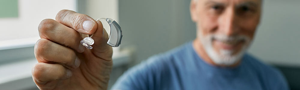 Senior man in blue shirt holds up hearing aid